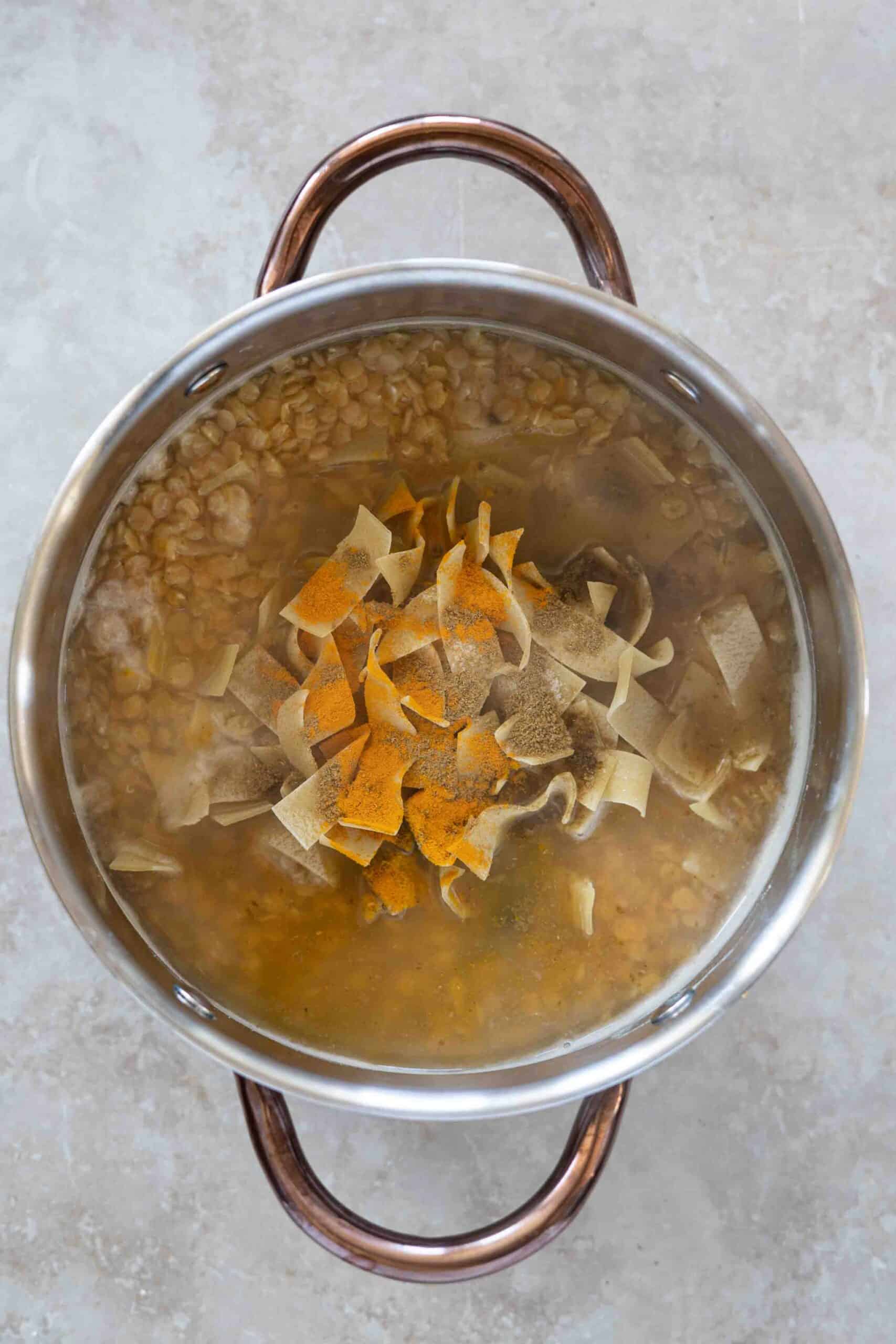 Pouring spices over lentils and pasta in a pot.