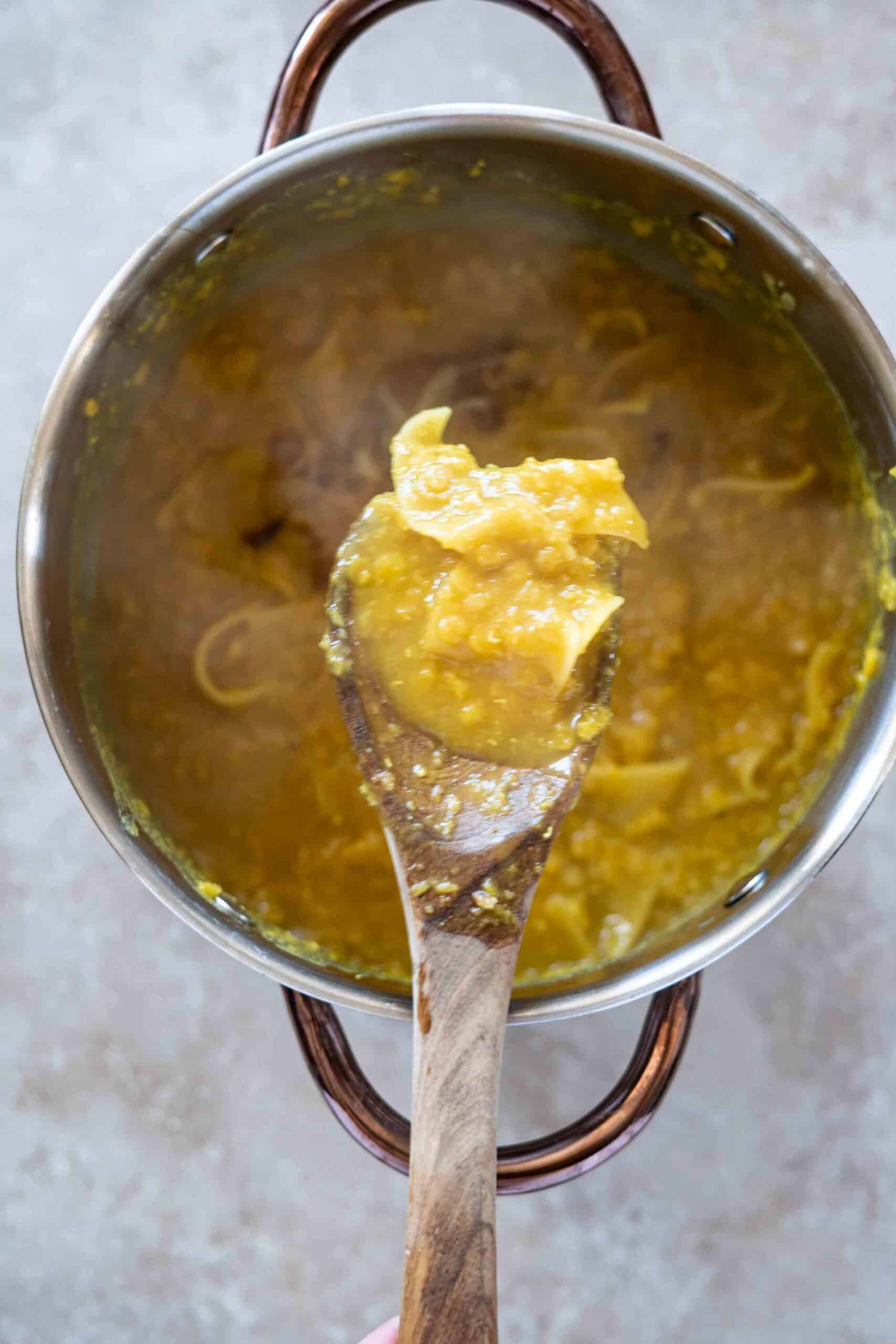 A close-up of a wooden spoonful of rishtayeh lifted from a pot.