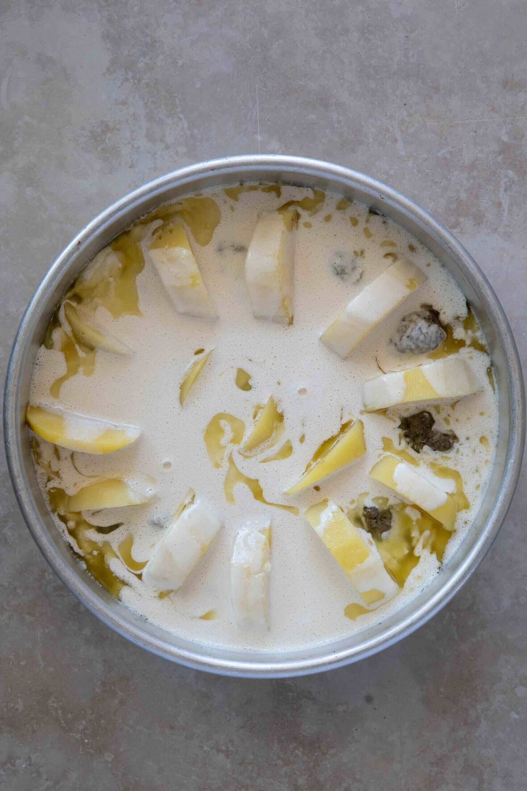 Kafta and potatoes covered in creamy tahini sauce in a baking dish before baking.