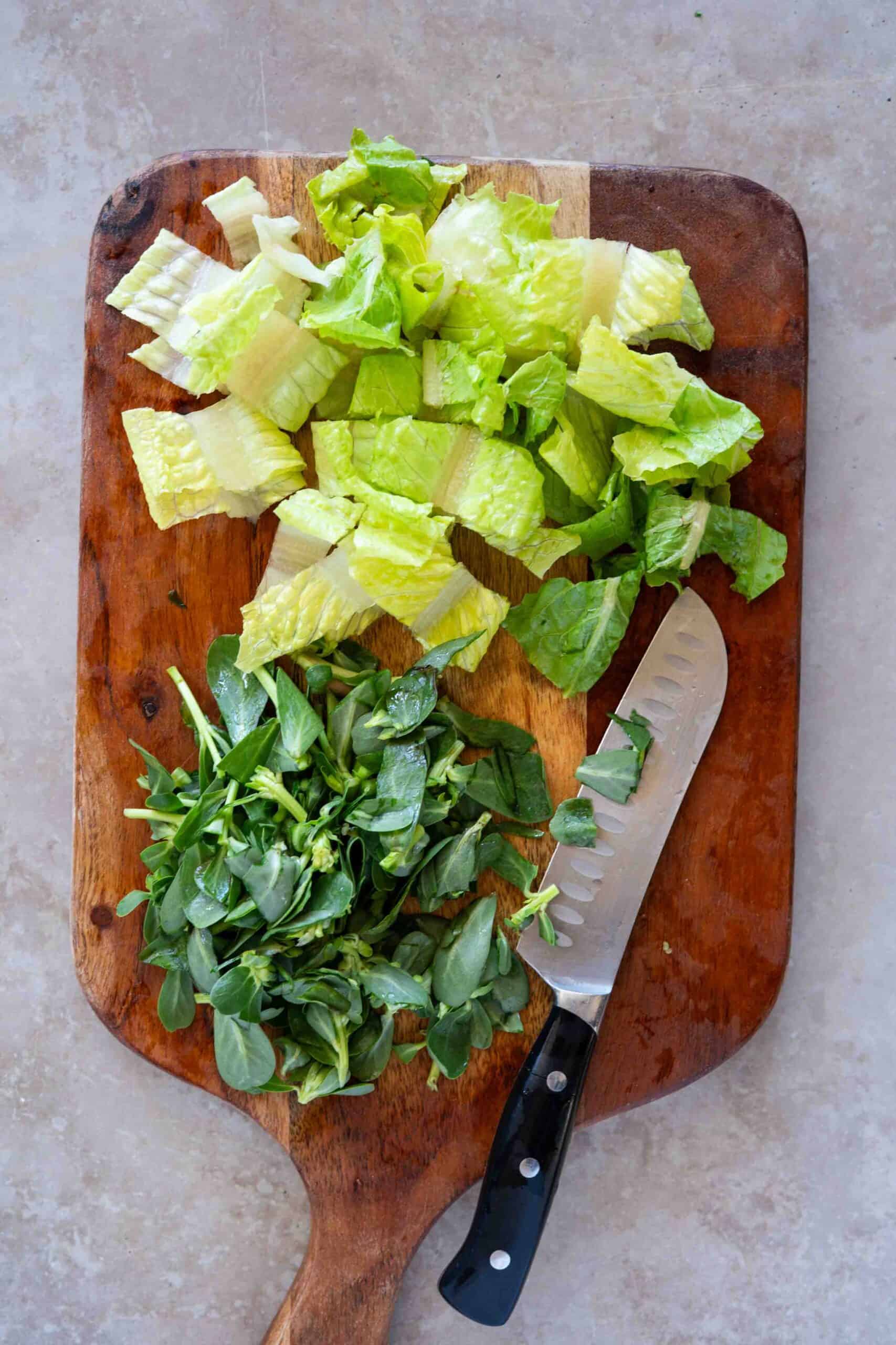 Roughly chopped romaine lettuce and purslane on a cutting board.