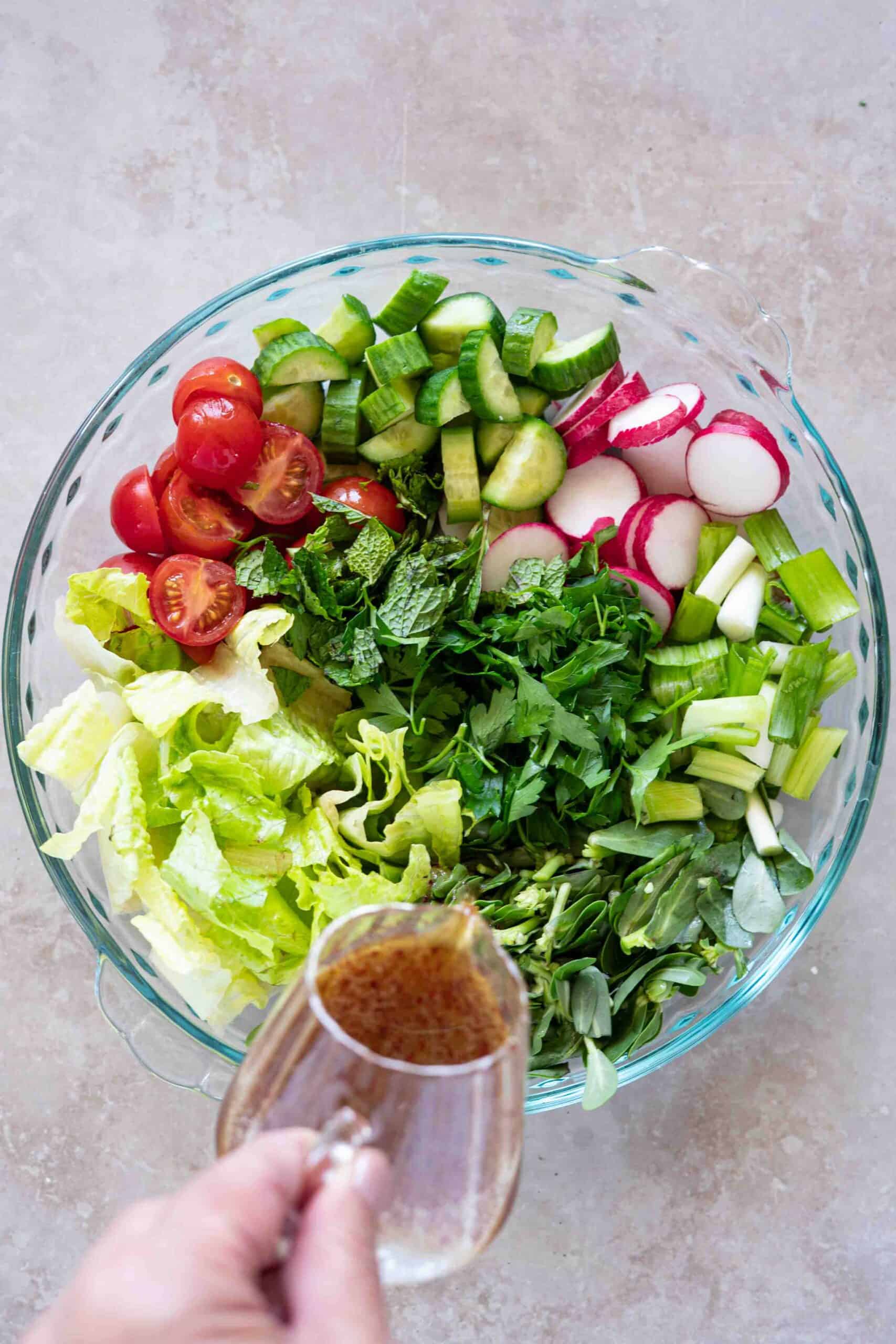 Pouring dressing over chopped vegetables and herbs