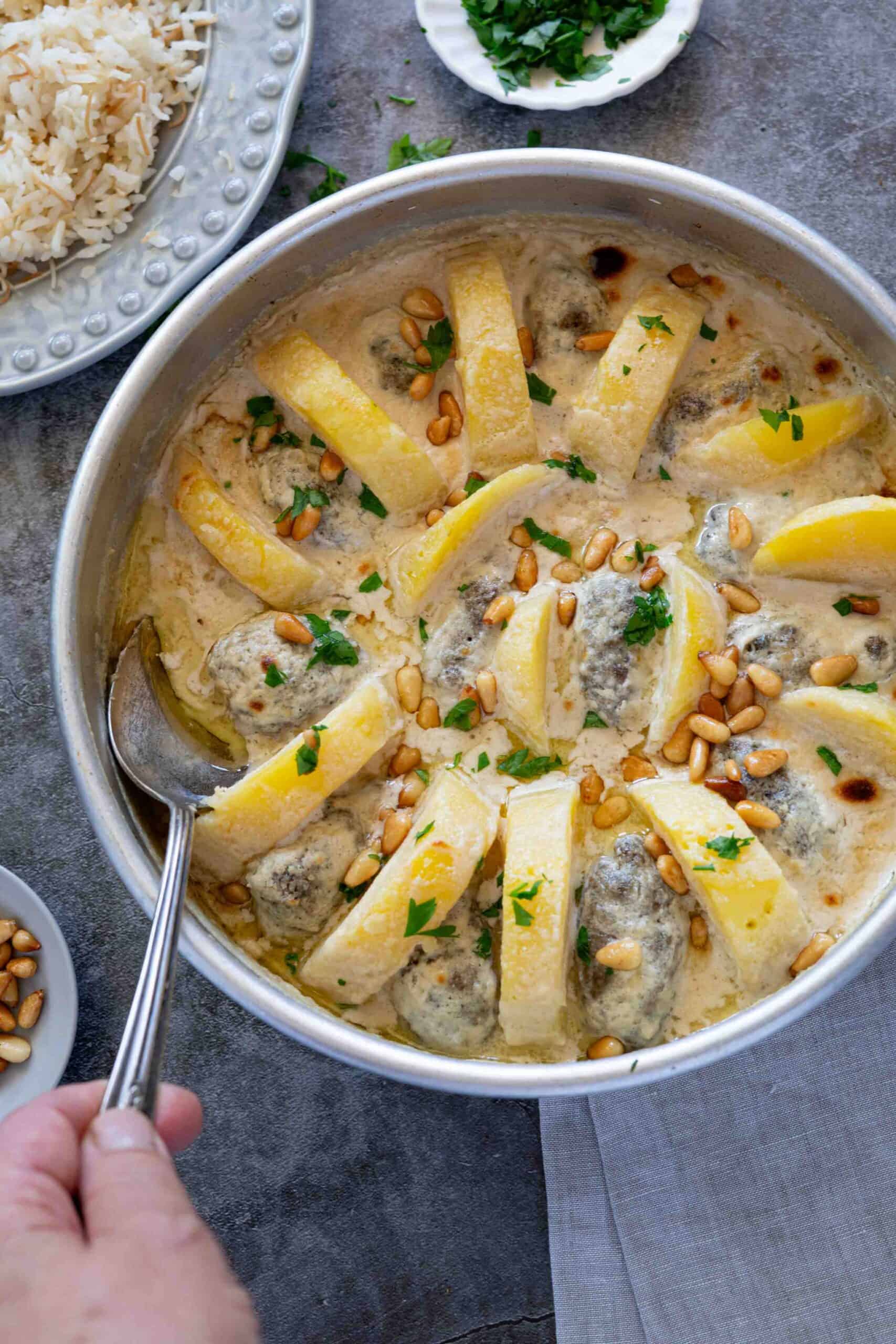 Close-up of a spoon dipped into rich, creamy tahini sauce baked with Palestinian kafta and potatoes.