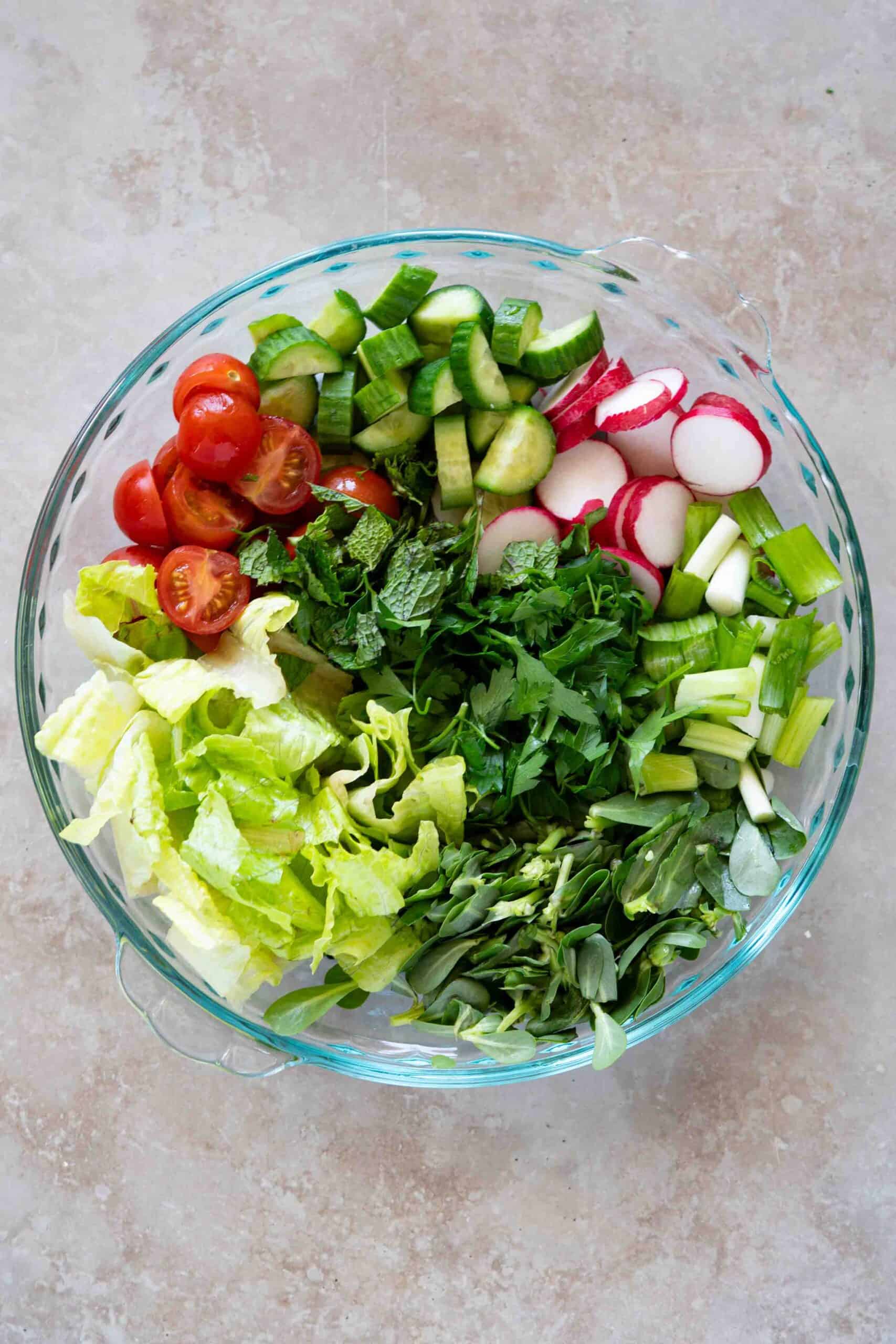 Chopped vegetables and herbs placed next to each other in a bowl.
