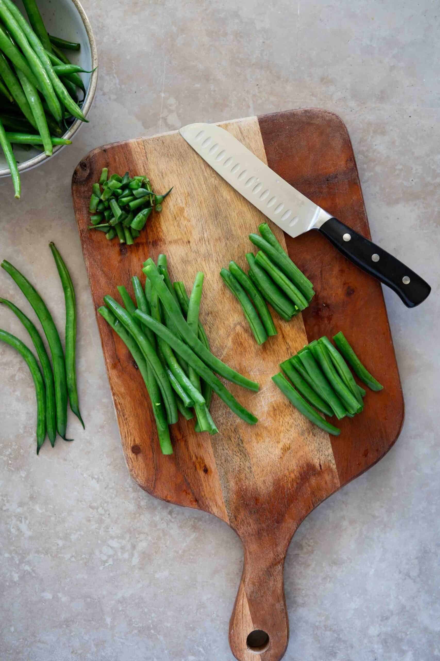 Removing stem from green beans and cutting each in half.