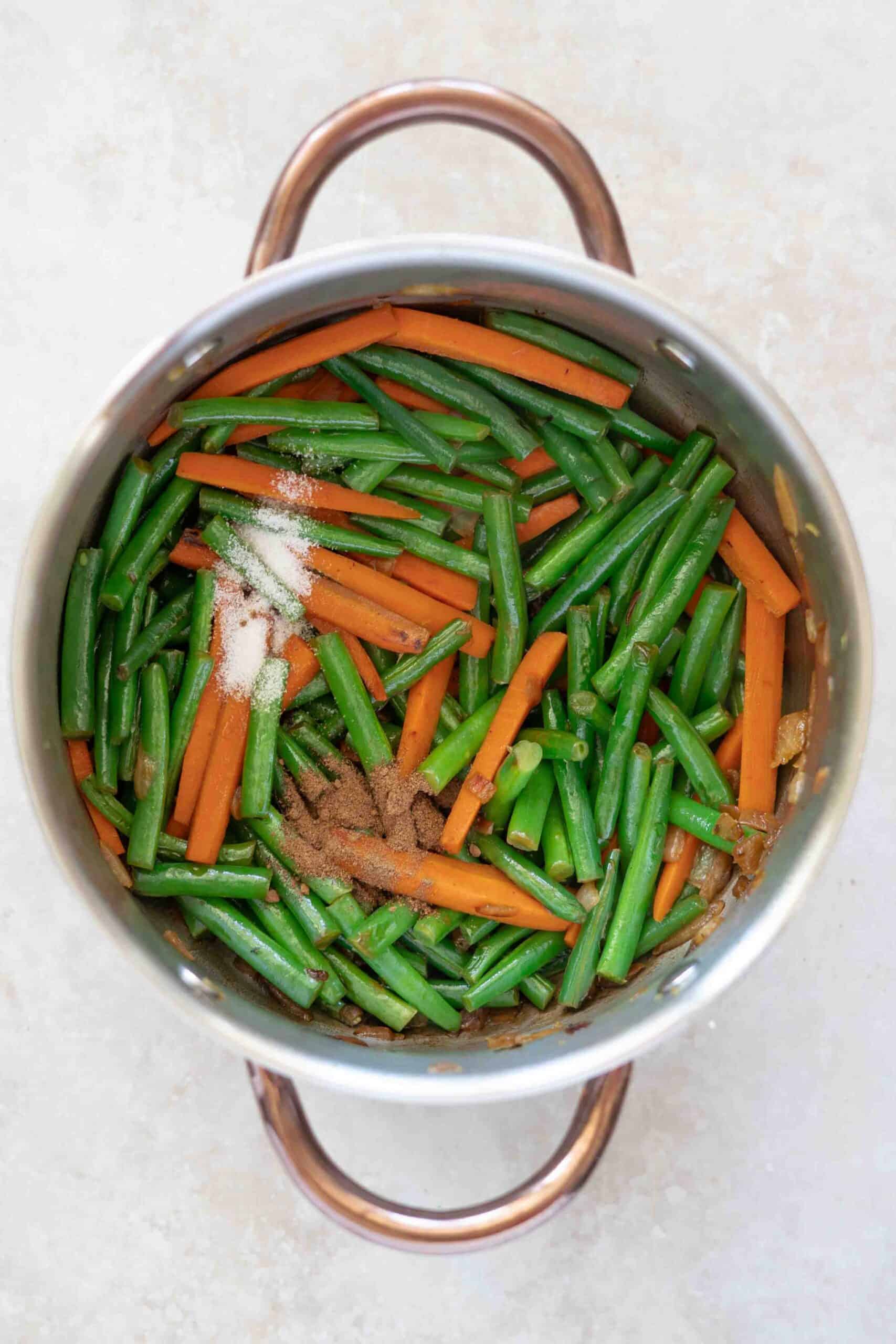 Adding spices over carrots and beans in pot
