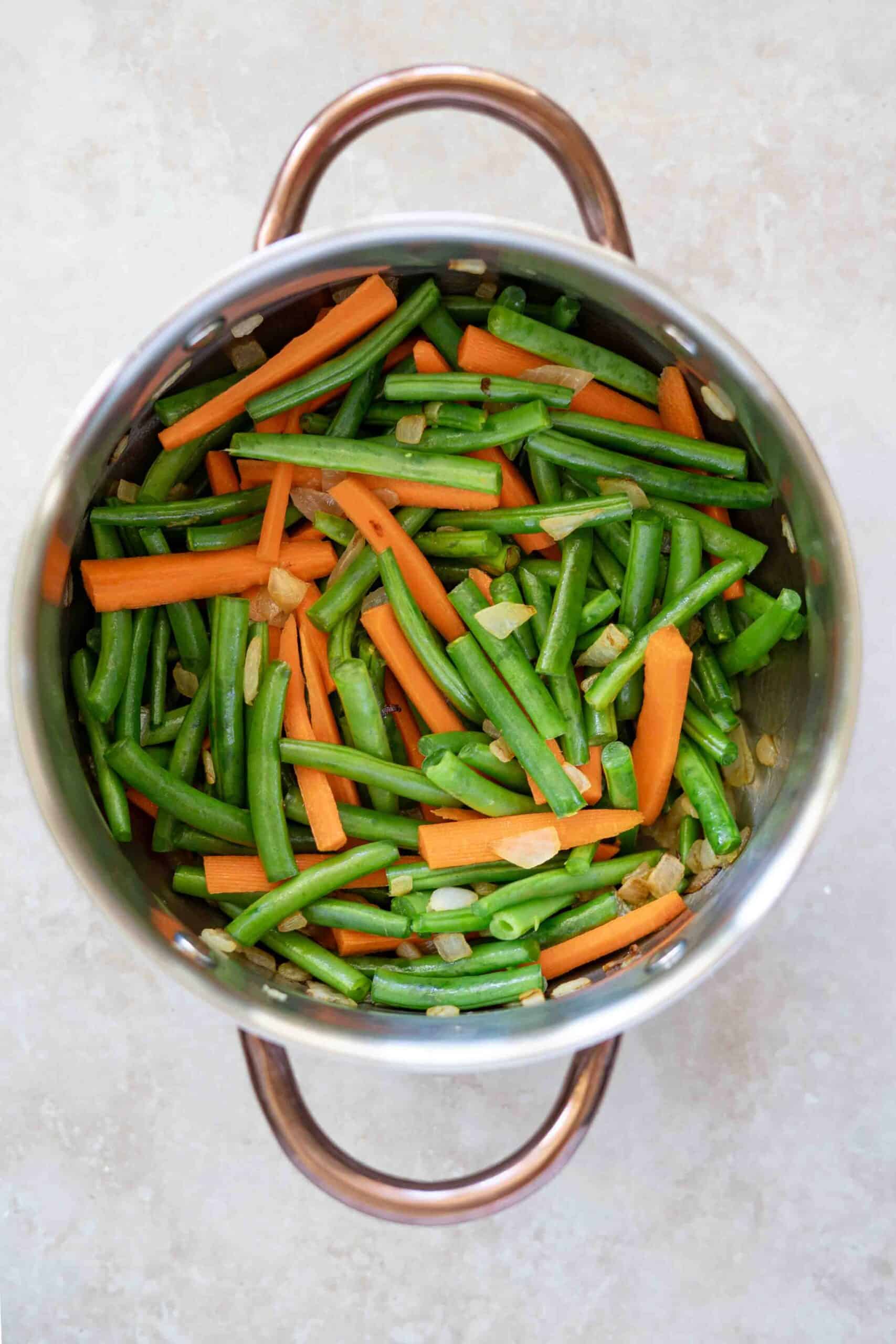 Carrots and beans in pot all mixed with caramelized onions ready to cook